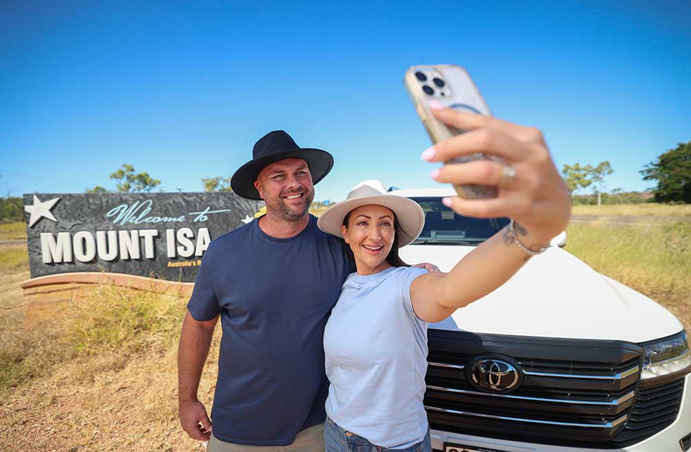 Man and woman pose for a selfie in front of the Welcome to Mount Isa sign.