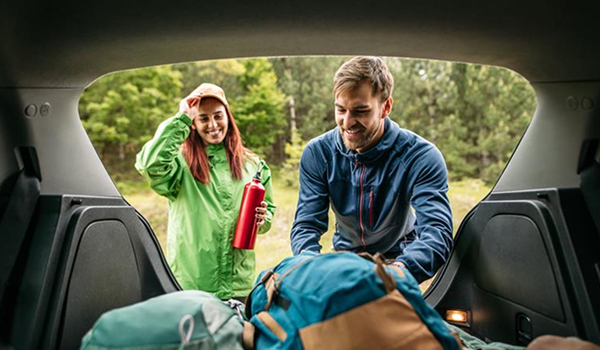 A man and woman preparing for a trip, loading camping gear into the back of a car